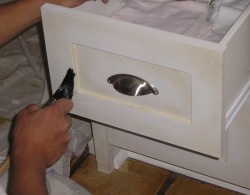 Finishing touches to a cabinet lightly antiqued using thinned stain over paint.