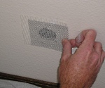 Placing metal drywall patch over hole in wall.