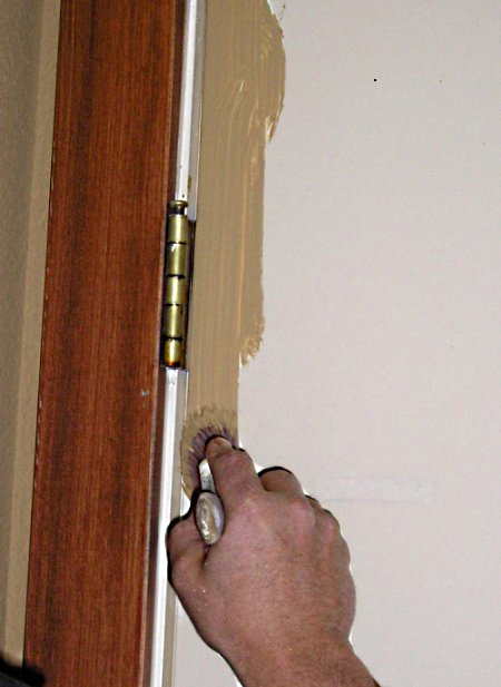 Applying paint with a brush next to a hinge of a steel door.