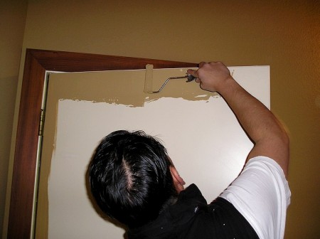 Applying paint with a roller to the top edge of a steel door.
